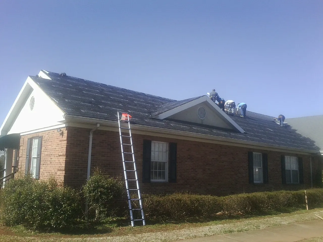 Crew tearing shingles off a brick ranch roof with a ladder set — Metal Roof Repair work by our crew in Keller