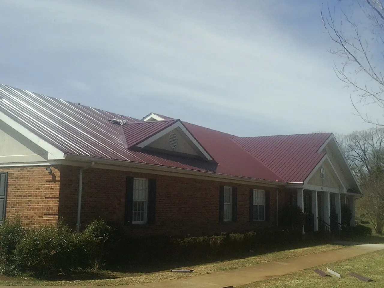 Red metal roof with gabled entries on a long brick building, from a Hail Damage Roof Repair job in Keller