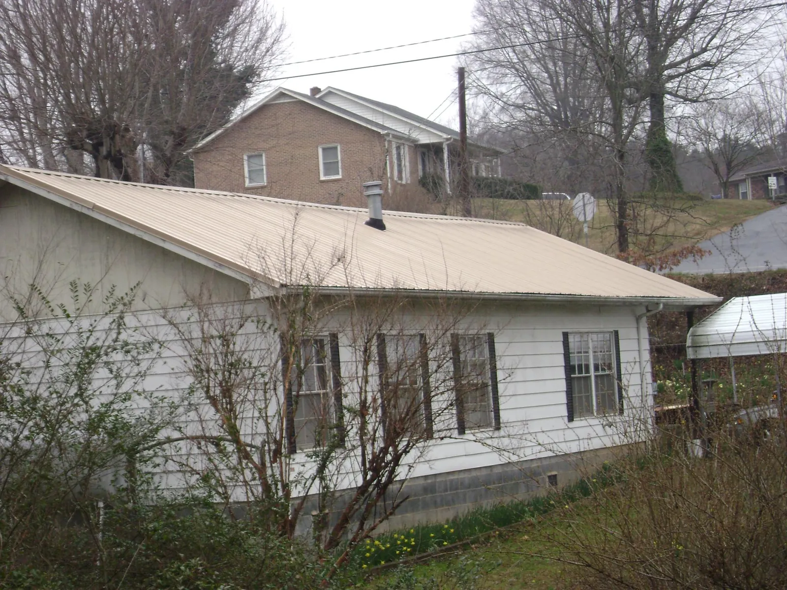 Tan metal roof on a white sided house set into a hillside — Commercial Roofing by Roofing Brothers in Keller